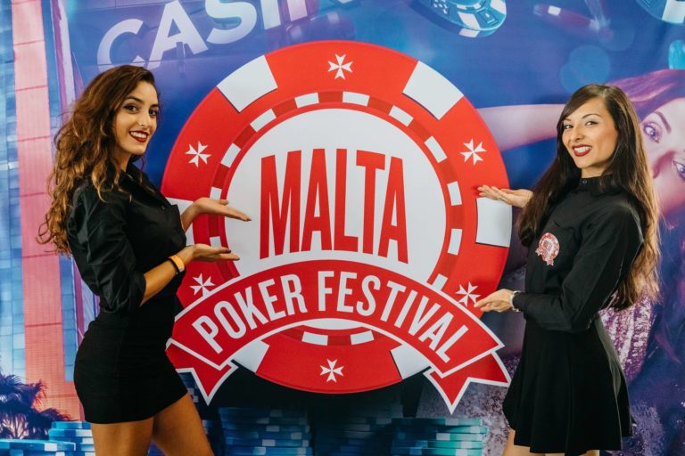 two girls in from of The Malta Poker Festival placard